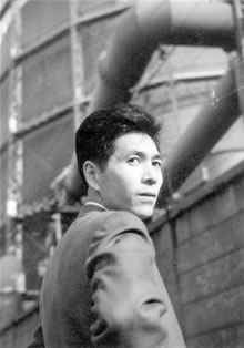 南千住のガスタンクを前に若き日の松本さんの写真