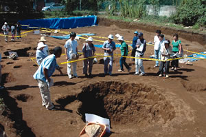市の担当者から地下式抗(手前の穴)について説明を受ける参加者の写真