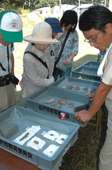 出土した陶磁器、土器、古銭、弾丸などを見る参加者の写真